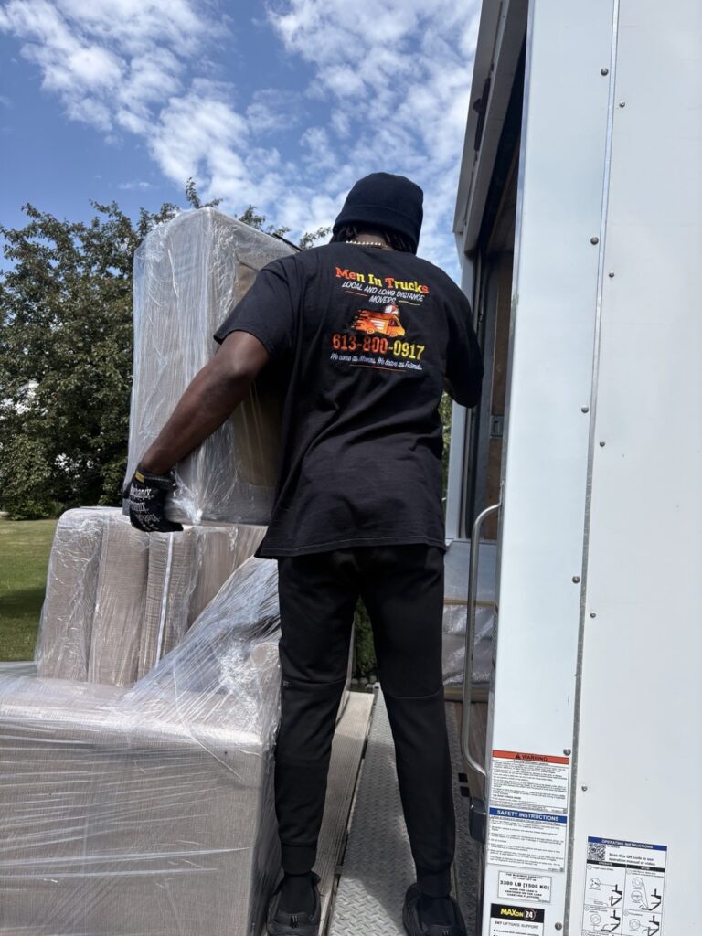 Mover in a Men In Trucks T-shirt loading a shrink-wrapped piece onto the truck’s liftgate.