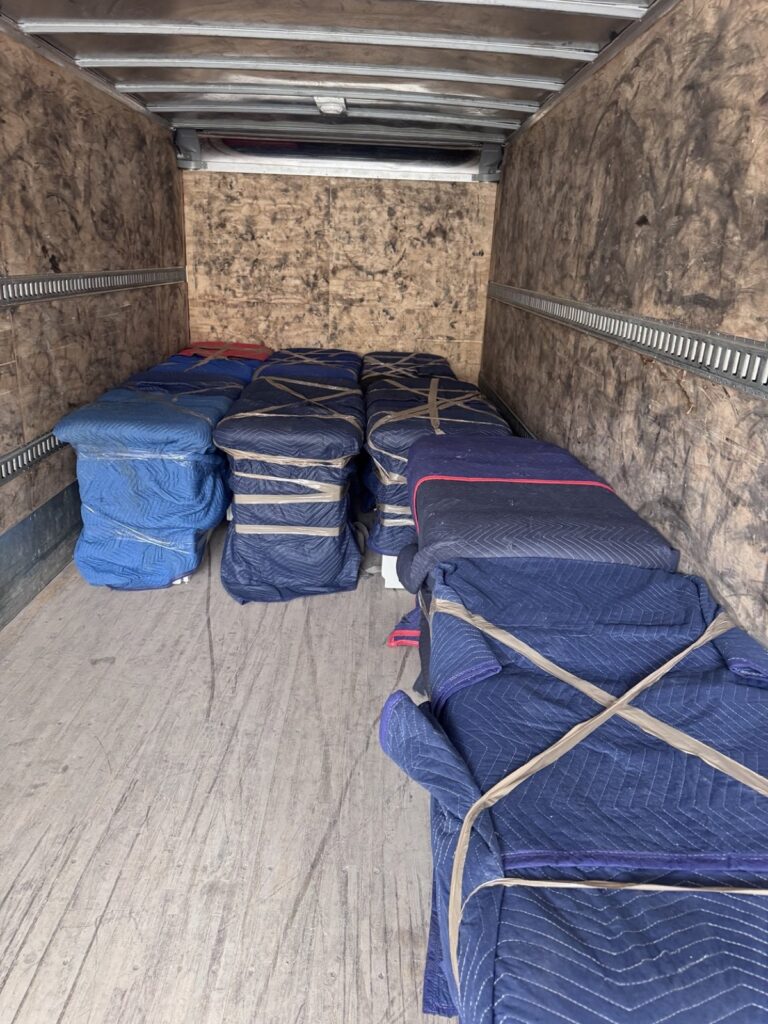 Inside a truck box: furniture wrapped in moving blankets, stacked and tied.