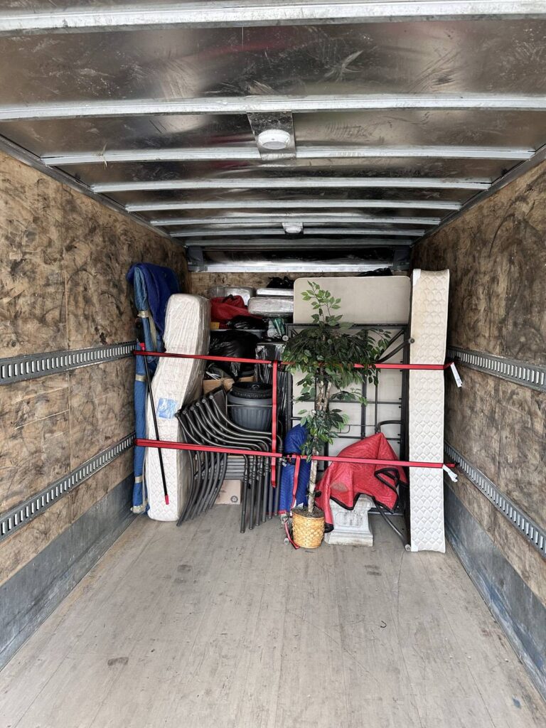 Furniture, a mattress and a plant held in place with red load straps inside a moving truck.